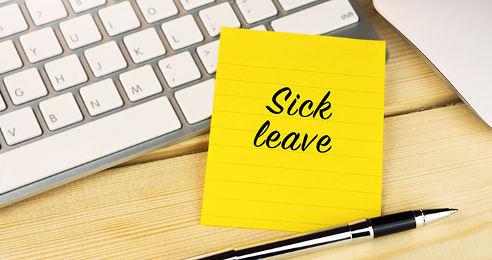 Sick leave written on a sticky note next to a keyboard and pen.